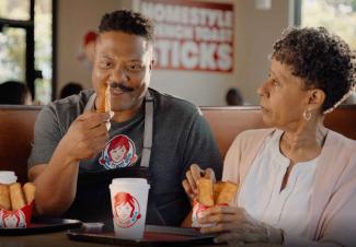 Wendy's commercial screenshot: Wendy's employee sitting at table eating French Toast Sticks with his mom